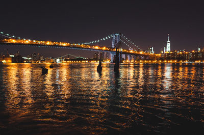 Illuminated bridge over river with city in background