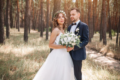 Smiling couple holding bouquet while standing in forest