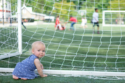 Full length of cute toddler sitting by net on playing field