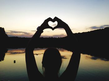 Silhouette woman standing by heart shape against sky during sunset