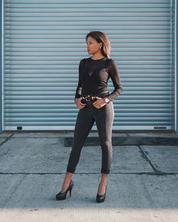 Full length portrait of young woman standing against wall