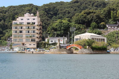 Buildings by river against trees