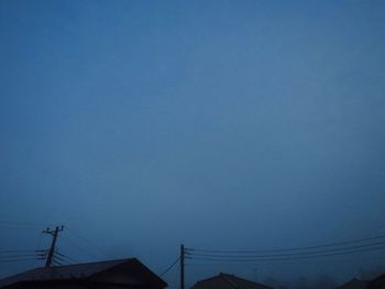 Low angle view of silhouette telephone pole against clear blue sky