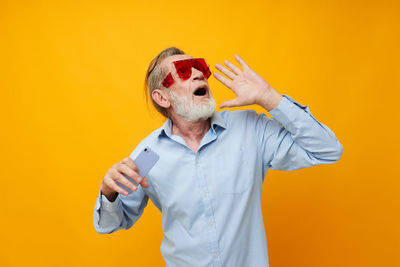 Young man suffering from mobile phone while standing against yellow background