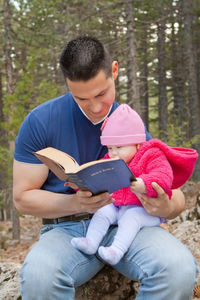 Rear view of man holding book while sitting on land