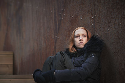 Young woman sitting against wall