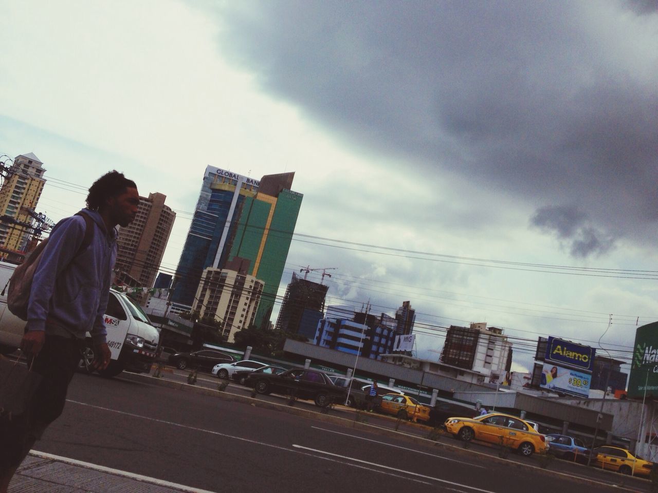 sky, building exterior, transportation, cloud - sky, architecture, city, built structure, street, cloudy, road, car, mode of transport, land vehicle, city life, cloud, railroad track, overcast, men, weather