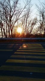 Road by bare trees against sky during sunset