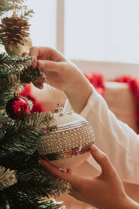 Crop female hanging elegant bauble on tree on christmas day at home person