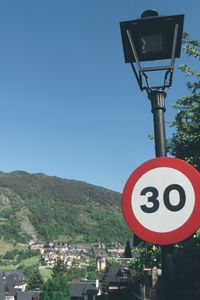 Road sign by city against clear blue sky