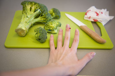 Cropped hand of woman with blood on finger by vegetables on cutting board