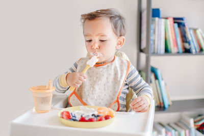 Baby boy eating ripe berries and fruits with yogurt. supplementary healthy food for toddlers kids.