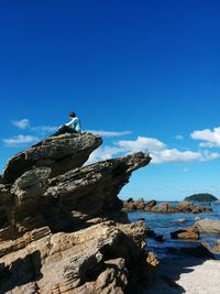 Low angle view of man sitting on rock formations against sky