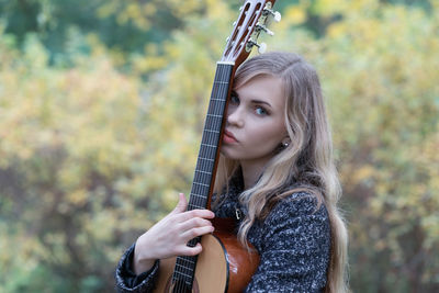 Portrait of beautiful young woman holding guitar outdoors