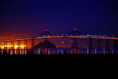 Illuminated city by sea against sky at night