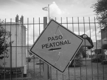 Information sign by fence in city against sky