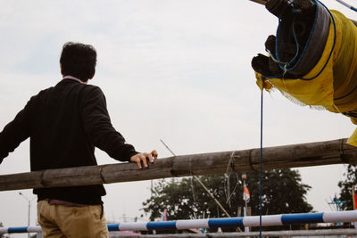 Rear view of man standing by railing against sky