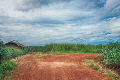 Dirt road amidst field against sky