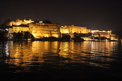 Illuminated buildings by river against sky at night