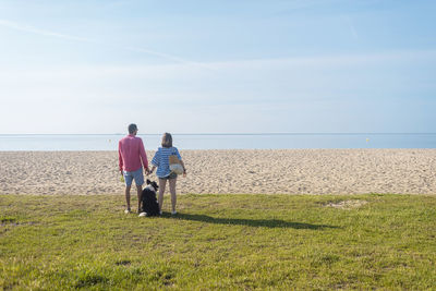 Back view of couple standing and holding hands near their dog on beach