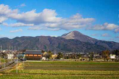 Scenic view of field by houses and mountains against sky