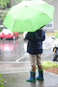 Low section of man with umbrella walking on wet road