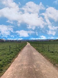 Empty road amidst field against sky