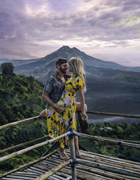 Young couple standing on railing against mountains