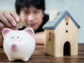 Man putting coin in piggy bank with model house on table