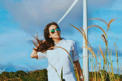 Young woman wearing sunglasses standing against sky