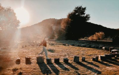 Side view of girl walking across wood stumps in a field at sunset 