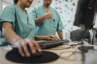 Midsection of nurse using computer by colleague at reception desk in hospital