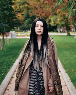 Portrait of young woman standing on footpath in park