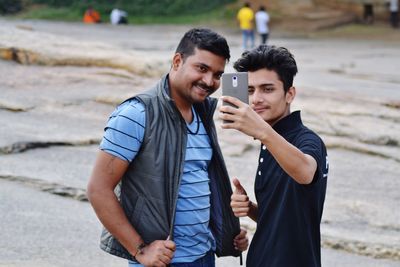 Portrait of young man holding camera while standing outdoors