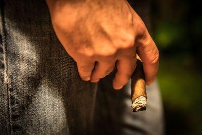 Midsection of man holding lit cigar