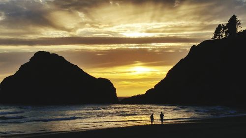 Silhouette people at beach against mountains and sky during sunset