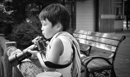 Boy with camera standing by bench in yard