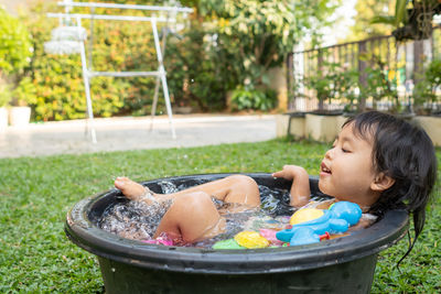 Cute little girl playing in round plastic wash basin during hot weather.