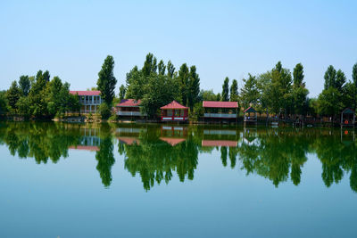 Reflection of trees and houses in lake against clear sky