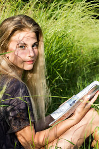 Portrait of beautiful woman with long blond hair while reading book on grassy field