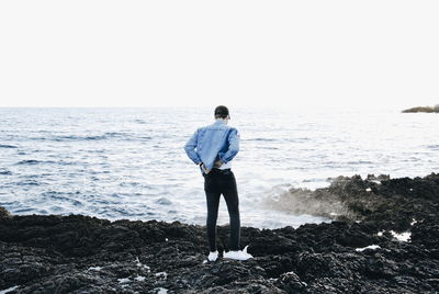 Rear view of man looking at sea against clear sky