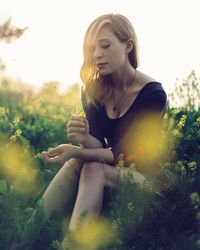 Young woman sitting on field against sky