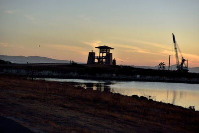 Silhouette factory against sky during sunset