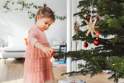 Side view of girl playing with christmas tree at home