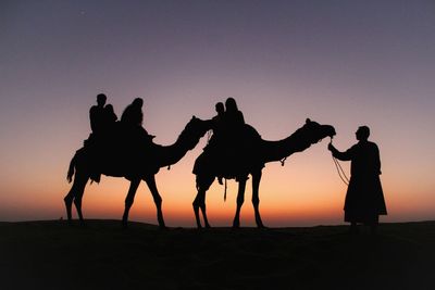 Silhouette of friends standing on sand at desert