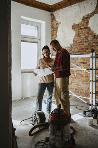 Couple discussing over blueprint in room while renovating home