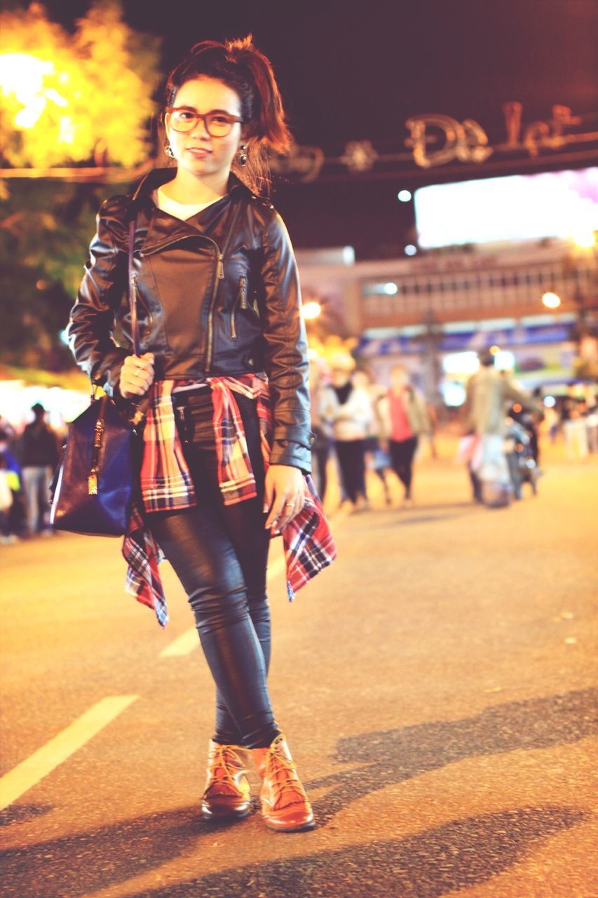 lifestyles, casual clothing, leisure activity, young adult, standing, focus on foreground, front view, person, full length, young women, street, looking at camera, portrait, happiness, night, enjoyment, three quarter length, incidental people