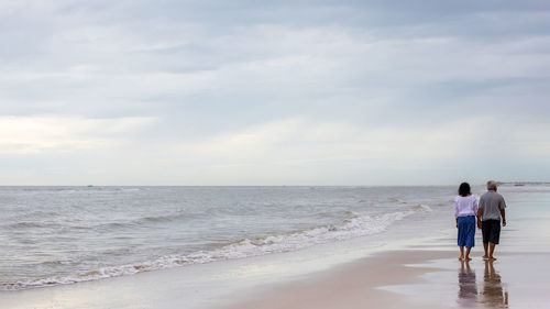 Rear view of people on beach against sky