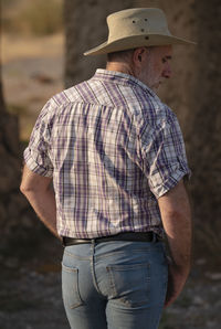 Rear view of adult man in cowboy hat and shirt against abandoned building