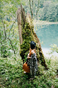 Rear view of woman sitting on tree trunk in forest